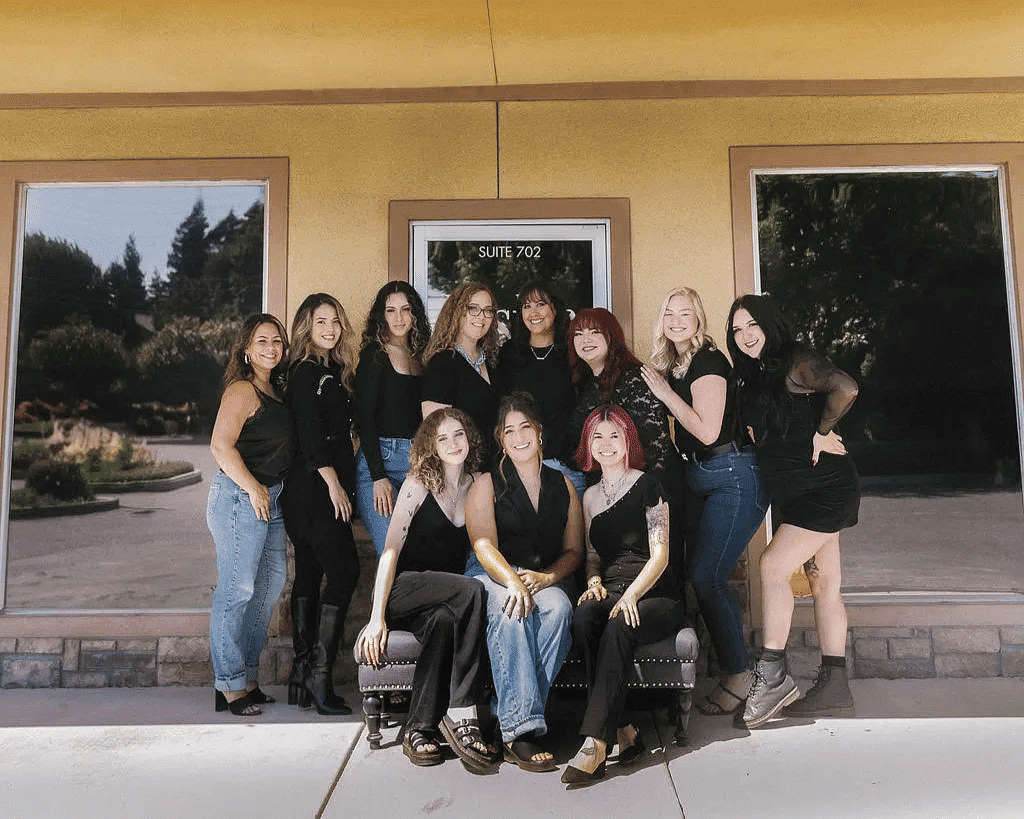 Group of twelve people posing in front of Luster Color Studio on a sunny day.