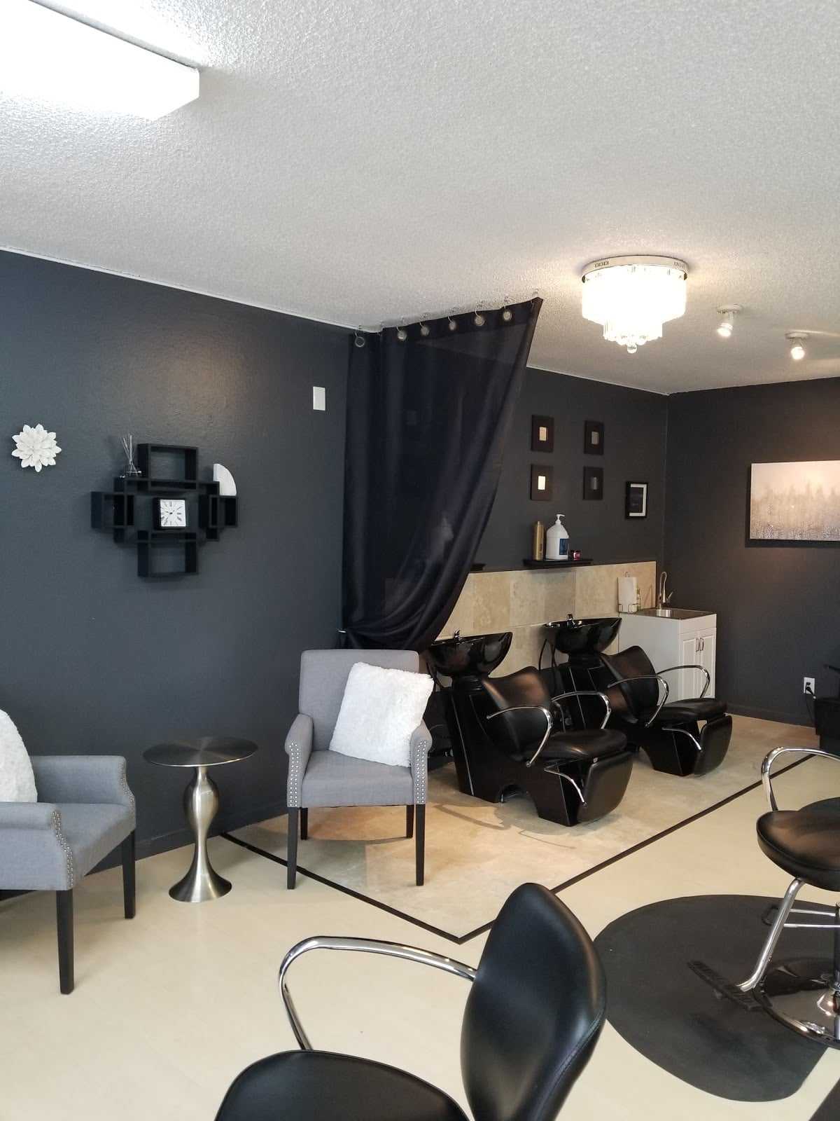 Modern hair salon with stylish black chairs, gray walls, and elegant lighting fixtures.