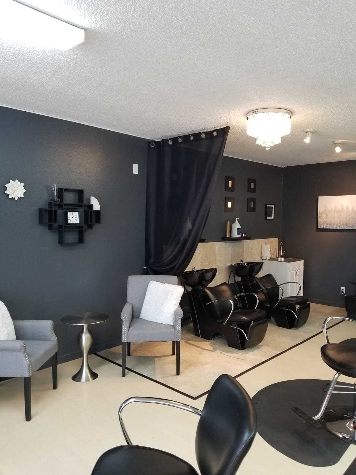 Modern hair salon with stylish black chairs, gray walls, and elegant lighting fixtures.